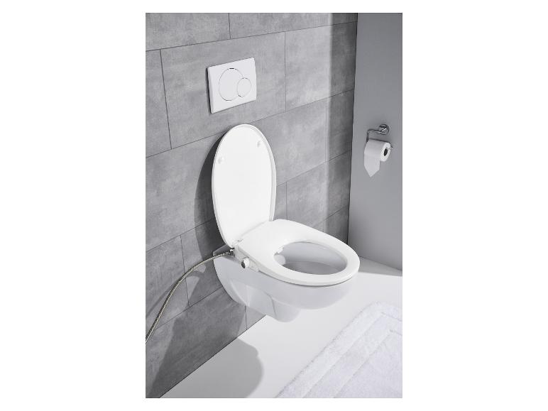 Une toilette blanche avec un siège de bidet, un porte-papier toilette et un bouton de chasse d'eau.
