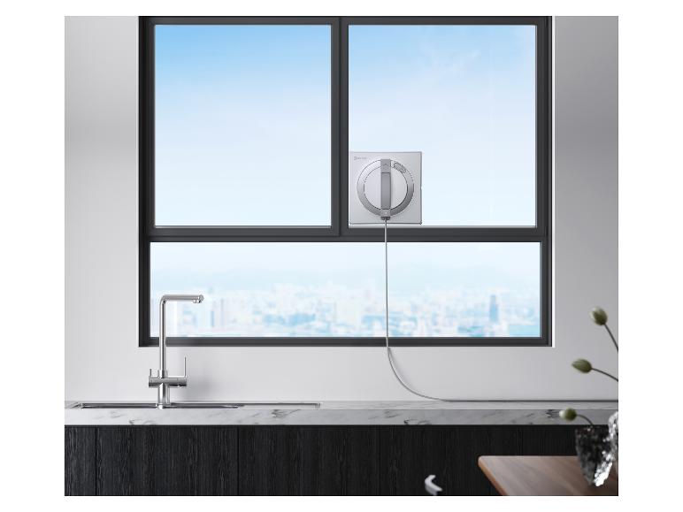 Robot nettoyeur de vitres sur une grande fenêtre avec vue sur la ville, au-dessus d'un évier de cuisine.