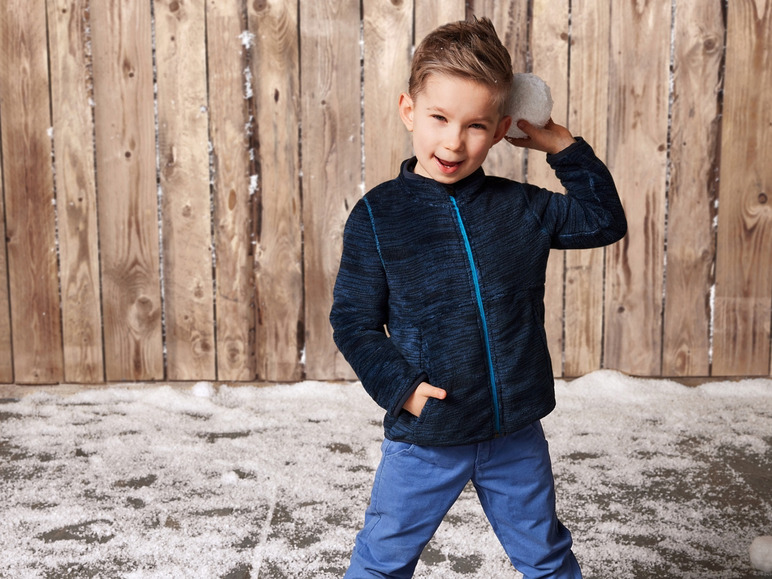 Un jeune garçon portant une veste bleue et un pantalon bleu tient une boule de neige.