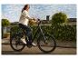 Jeune femme en veste en jean et jean foncé roulant à vélo électrique dans une rue résidentielle.