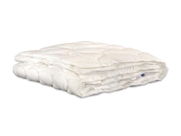 Une couette blanche matelassée pliée sur un fond blanc.