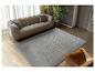 Salon moderne avec un canapé gris, un tapis texturé et un fauteuil en cuir.