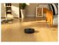 Robot aspirateur noir nettoyant un parquet dans un salon ensoleillé.
