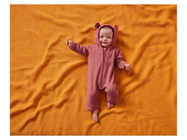 Bébé souriant en combinaison d'ours rose, allongé sur une couverture orange.