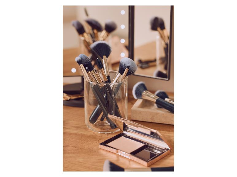 Pinceaux de maquillage dans un pot en verre et une poudre compacte sur une coiffeuse en bois.