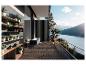 Balcon moderne avec plantes en pot, canapé et plancher en bois, donnant sur un lac et des montagnes.