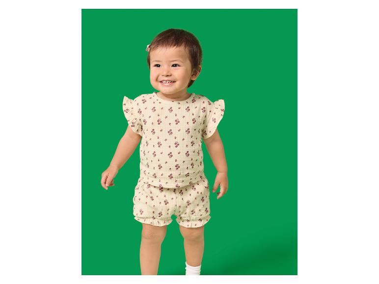 Bébé souriant dans un ensemble clair à motif floral, chemise et short.