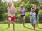 Une fille court en tête avec un t-shirt rouge et blanc à rayures, suivie de trois autres enfants dans un jardin vert.
