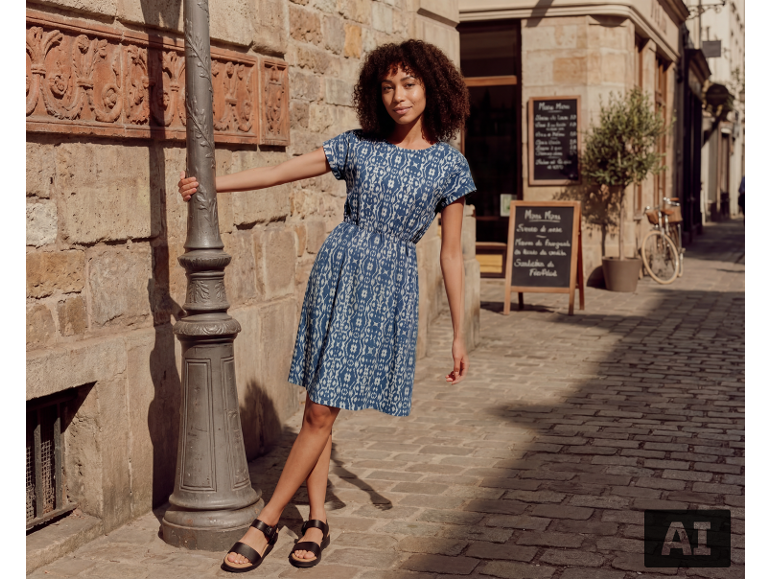 Femme en robe bleue à motifs et sandales noires dans une rue pavée.