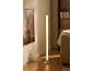 Lampadaire cylindrique avec base chromée éclairant un salon moderne avec étagère et canapé.