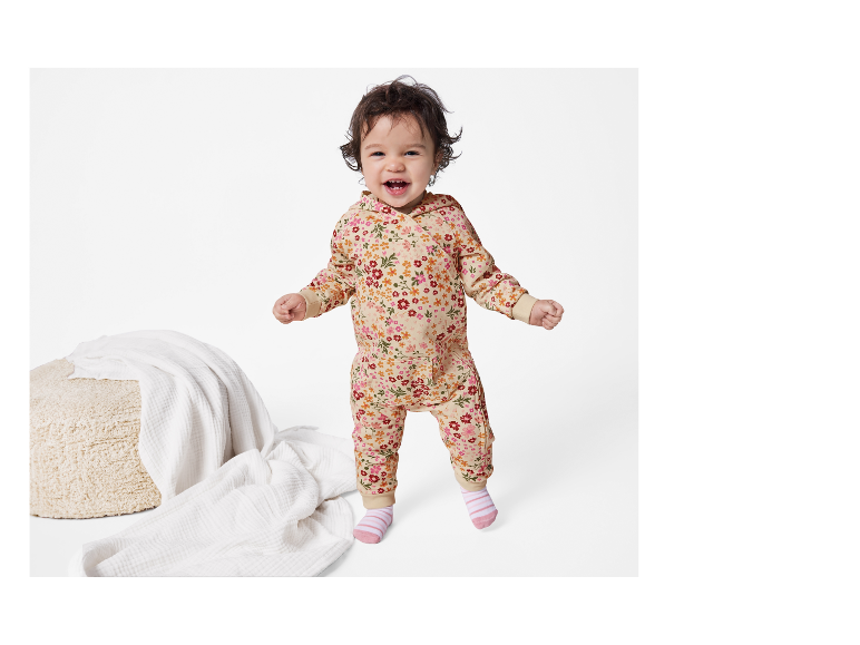 Bébé souriant portant une combinaison à capuche fleurie.