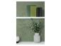 Livres verts et vase avec eucalyptus sur étagères blanches contre un mur vert.