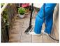 Personne nettoyant les carreaux de balcon avec un balai vapeur, avec des plantes en pot à proximité.