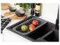 Évier de cuisine noir avec égouttoir gris contenant des fruits, à côté d'une planche à découper.