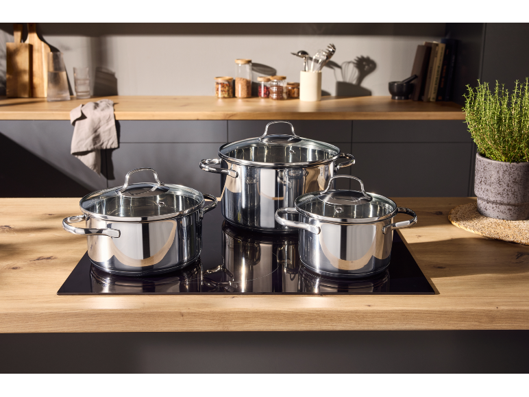 Trois casseroles brillantes avec couvercles en verre sur une plaque de cuisson dans une cuisine moderne.