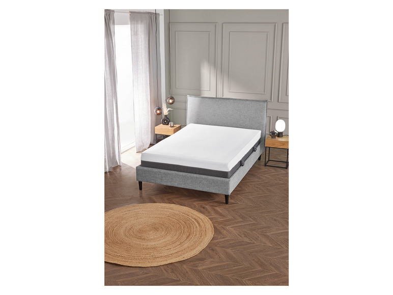 Un cadre de lit gris avec un matelas blanc dans une chambre à coucher moderne.