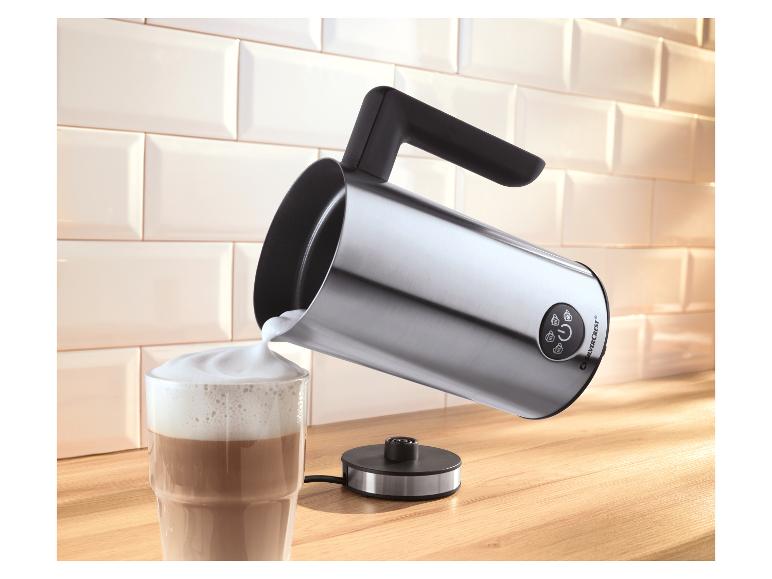 Mousseur à lait versant du lait moussé dans un verre de café sur un comptoir en bois.