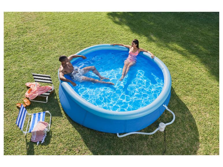 Couple se relaxant dans une piscine gonflable bleue, avec chaises longues et serviettes sur l'herbe.