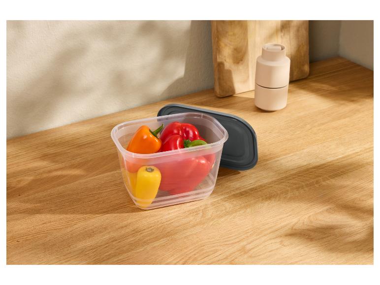 Poivrons dans un récipient en plastique avec couvercle gris foncé sur un comptoir en bois.