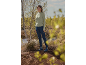 Femme en pull vert, jean bleu foncé et bottes bleues dans la nature.