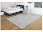 Un tapis gris doux avec un motif en losanges dans une chambre à coucher avec un lit.