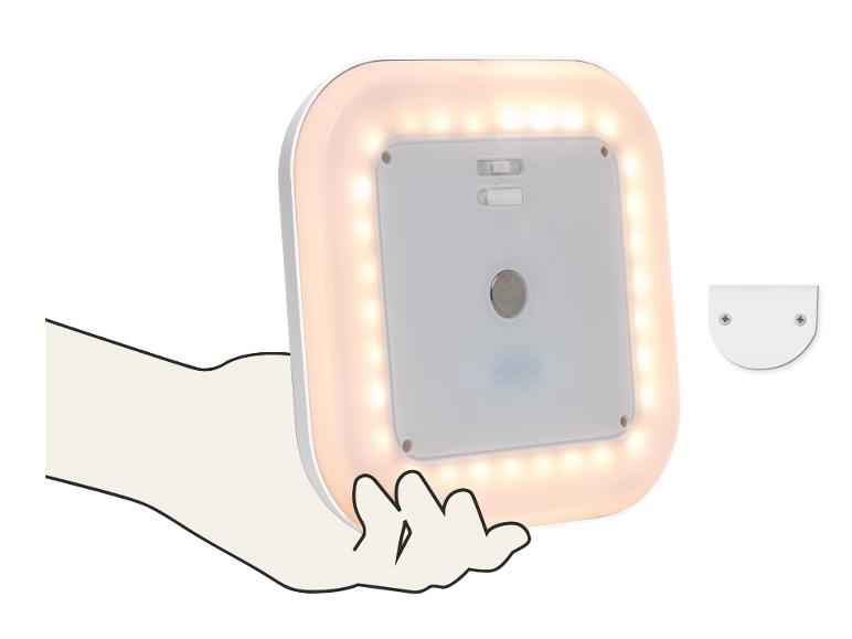 Lampe LED carrée à lumière blanc chaud, tenue par une main, avec un support de montage à côté.