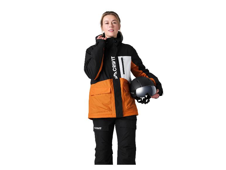 Femme en veste et pantalon de ski orange et noirs, tenant un casque.