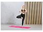 Femme faisant du yoga sur un tapis rose avec un soutien-gorge de sport et un legging noirs.