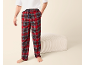 Homme portant un pantalon de pyjama écossais rouge et un t-shirt blanc, debout à côté d'un pouf beige.