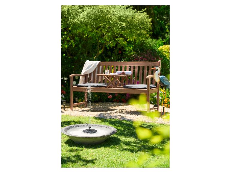 Banc de jardin en bois avec table intégrée, coussins, fontaine solaire et décor d'oiseau.