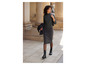 Une femme porte un pull gris, une jupe et des bottes noires.