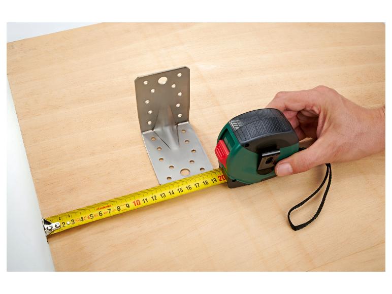 Mesure d'une planche en bois avec un mètre ruban à côté d'un support métallique.