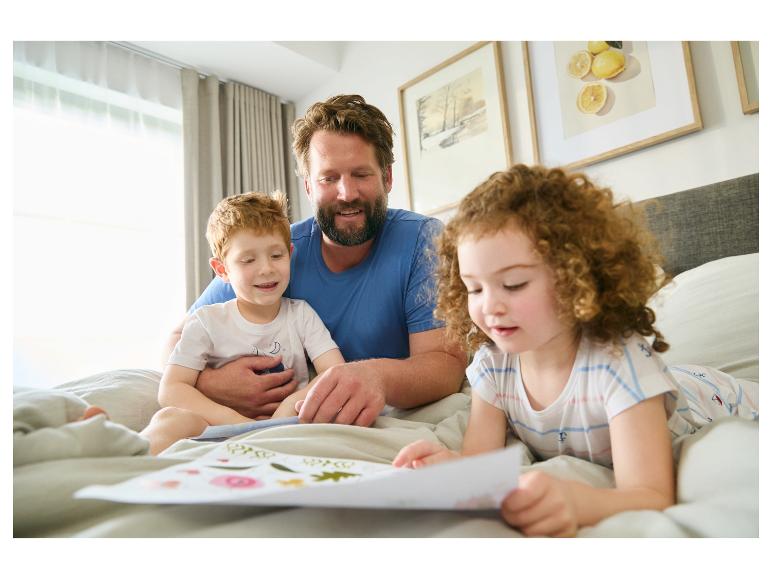 Père et enfants lisant un livre d'images au lit.