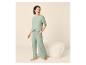 Femme en pyjama vert clair avec pantalon et T-shirt, debout à côté d'un pouf.