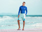 Un homme portant un rashguard bleu et un short bleu avec le logo 'mi' sur la plage.