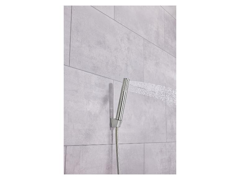 Pommeau de douche chromé pulvérisant de l'eau sur un mur carrelé gris clair.