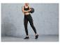 Femme en leggings noirs et haut de sport tenant un ballon d'entraînement.