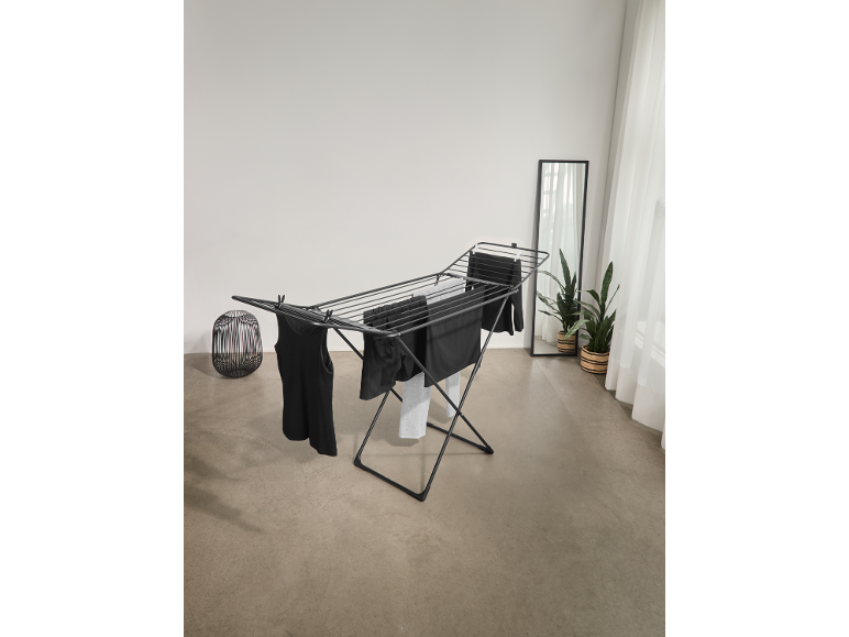 Séchoir à linge noir avec des vêtements sombres dans une pièce lumineuse.