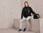 Une femme porte un sweat-shirt noir Jette Joop, un pantalon de jogging gris et des baskets noires.