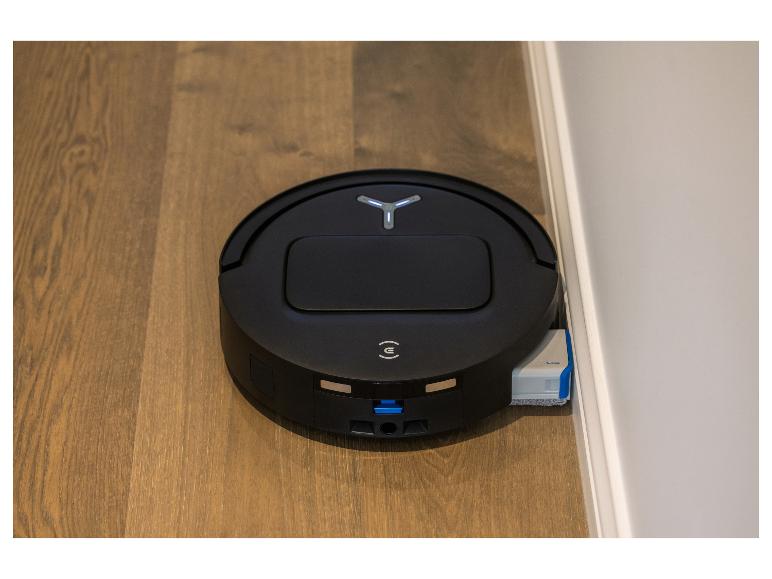 Aspirateur robot noir avec fonction serpillière, marqué 'TruEdge', sur un parquet près d'un mur.