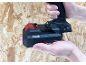 Mains tenant une perceuse sans fil avec une batterie 2.0Ah sur fond de bois.