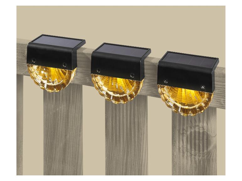 Trois lampes solaires de clôture à lumière jaune chaude fixées sur une clôture en bois.