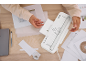 Une personne plastifie et coupe du papier avec une plastifieuse blanche sur une table en bois.
