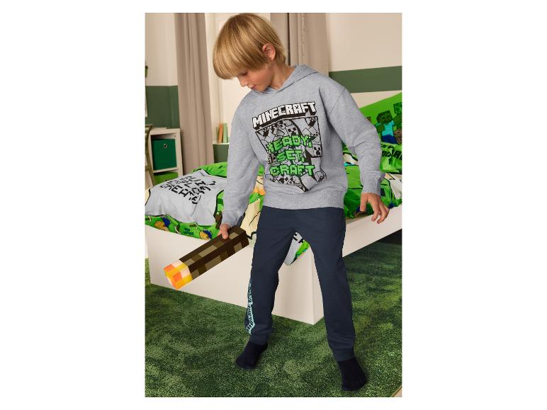 Garçon en sweat à capuche Minecraft et pantalon bleu marine, tenant une torche Minecraft.
