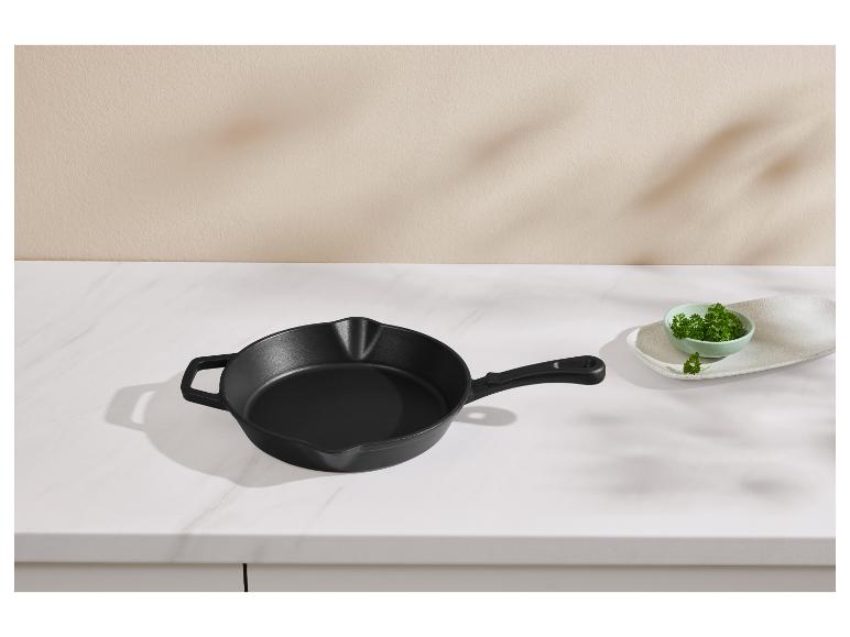 Poêle en fonte noire sur un comptoir en marbre avec un bol de persil.