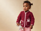 Un bébé porte une veste en polaire rouge et tient un lapin en peluche.
