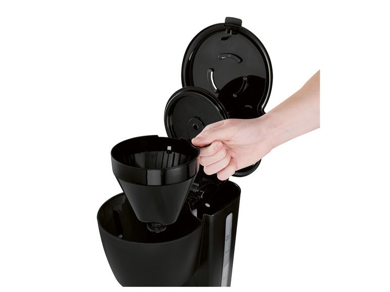 Une main plaçant un filtre à café dans une cafetière noire.