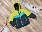 Une veste d'hiver verte et bleue pour enfants sur un sol en bois avec de la fausse neige.