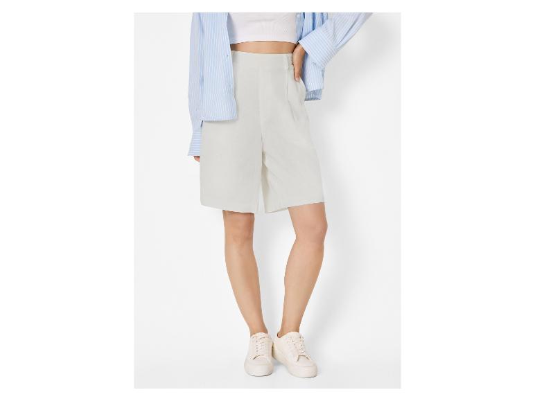 Femme en short gris clair, crop top blanc, chemise rayée bleue et baskets blanches.