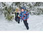 Deux garçons en combinaisons et vestes d'hiver courent dans la neige près des sapins.